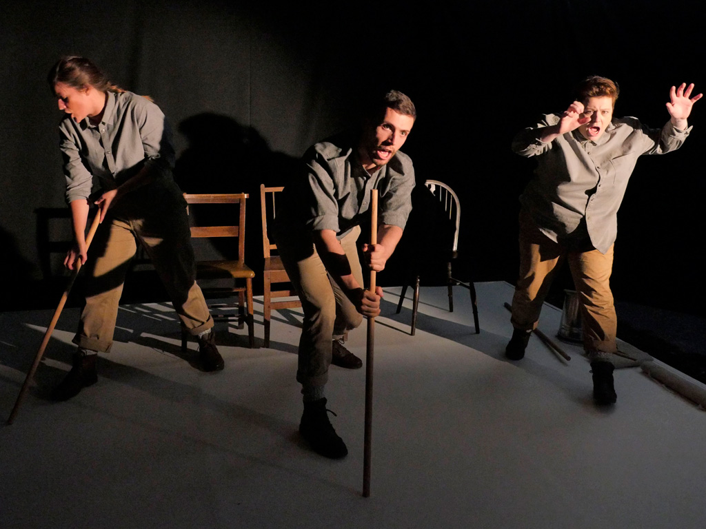 Performers on a stage with sticks in front of 3 chairs. 