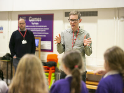 Cap-a-Pie Facilitator Brad McCormick stands with his hands apart at chest level in front of school students.