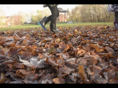 child wearing wellies walks across fallen leaves