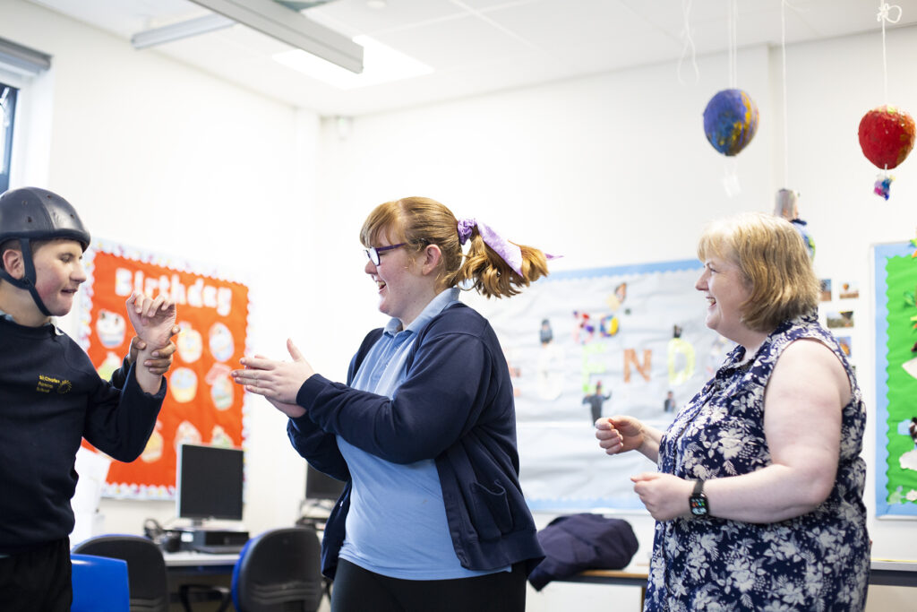 School students and staff smiling and passing a clap to each other. 
