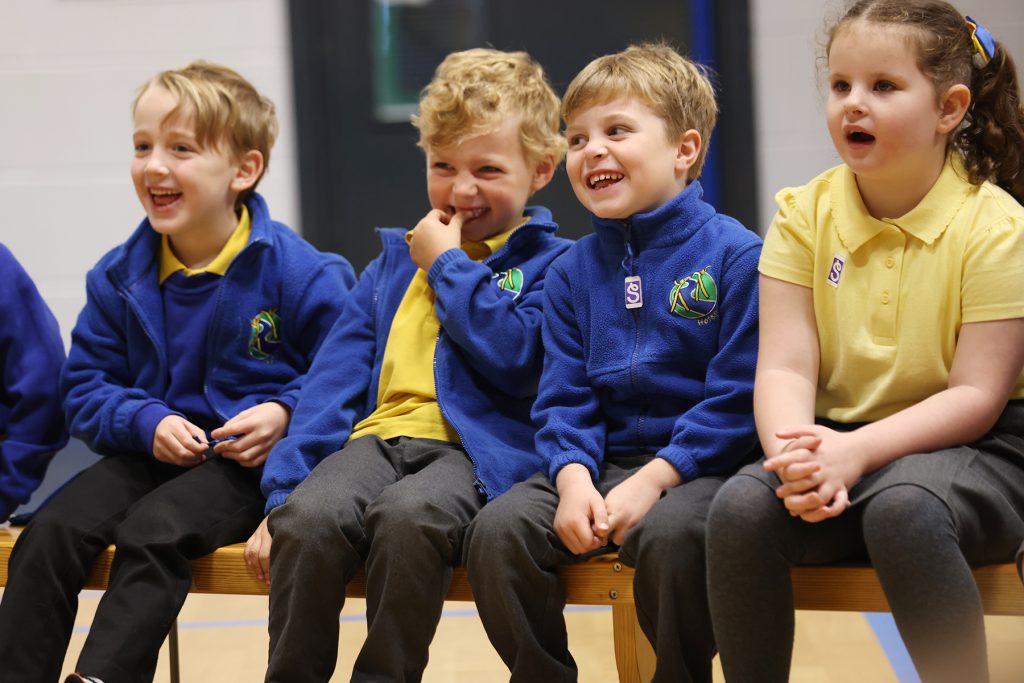 A group of children laugh as they take part in drama activities.
